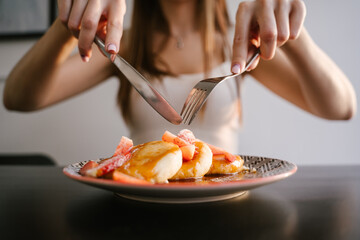 Female beautiful hands hold a fork and a knife, a cut of curd pancakes