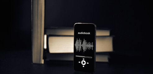 Audio book education. Phone screen with audio book app on paper books black background. Online...