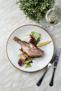 Whole pike fish roasted with herbs, served with a glass of white wine, directly above view, copy space, light and elegant photo