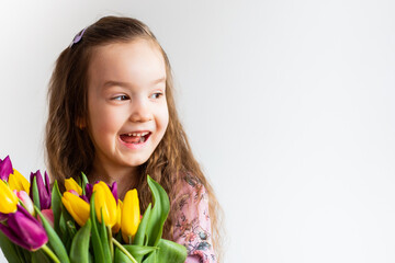 Fototapeta premium cute girl on a white background with bright flowers tulips. She smiles beautifully.
