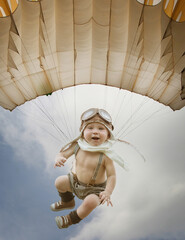 Child pilot. A kid in the form of a pilot flies on a parachute against the blue sky. The kid...