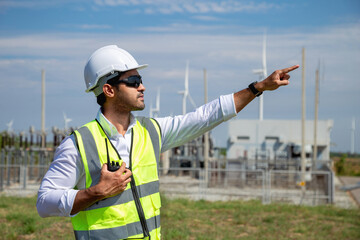 A male engineer in white helmet pointing his finger standing in wind turbine power generator...