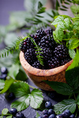 Freshly assorted berries in wooden bowl. Juicy and fresh blueberries6 blackberries and raspberries with green leaves on rustic background. Concept for healthy eating and nutrition.
