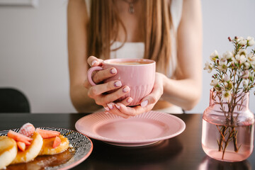 Woman's hand holds a pink mug with coffee, breakfast in a coffee shop