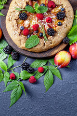 Whole-grain galette with plums and berries on dark background, top view