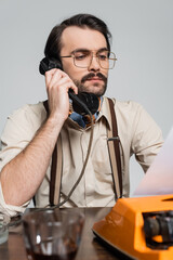 journalist in eyeglasses talking on retro phone and looking at paper in typewriter isolated on grey.