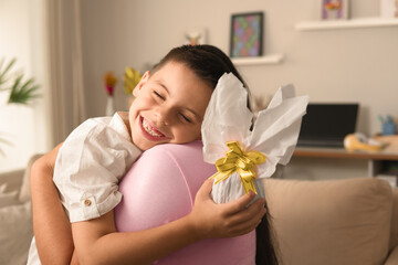 Happy brazilian kid with easter egg hugging woman at home