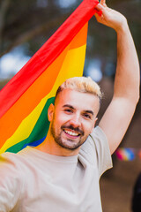 Gay man holding rainbow lgbt flag with a smile, vertical format