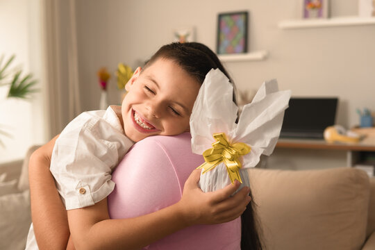 Happy brazilian kid with easter egg hugging woman at home