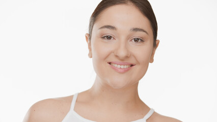 Close up shot of young plus size woman with long dark hair in ponytail in white top smiling wide for the camera on white background | Smooth armpit concept