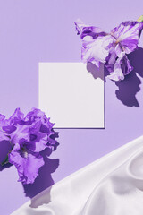 Empty card note with iris flower on pastel violet background with white silk cloth. Nature concept....