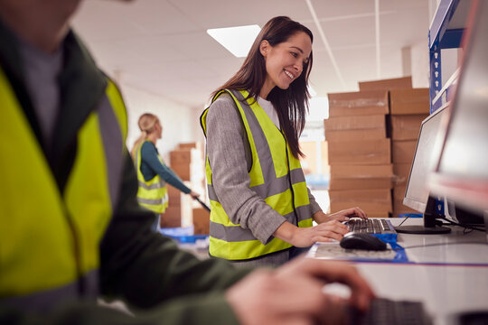 Staff In Busy Modern Warehouse Working On Computer Terminals