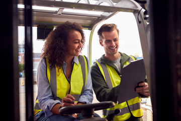 Male And Female Staff Operating Fork Lift Truck In Modern Warehouse