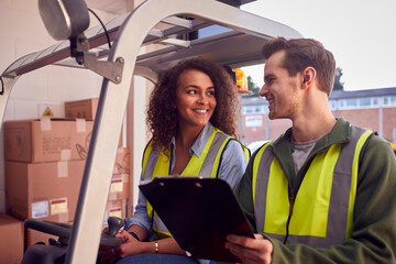Male And Female Staff Operating Fork Lift Truck In Modern Warehouse