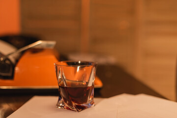 glass of whiskey near typewriter machine on desk.