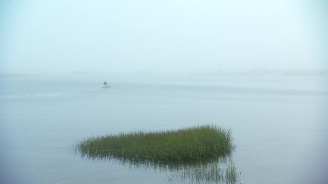 Wide shot of man rowing a row boat into the eerie Maine fog.