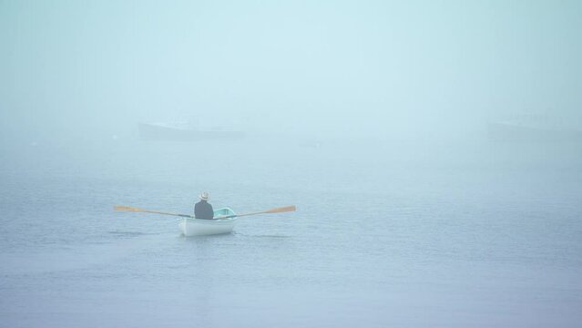 Closeup of man rowing a row boat into the eerie Maine fog.