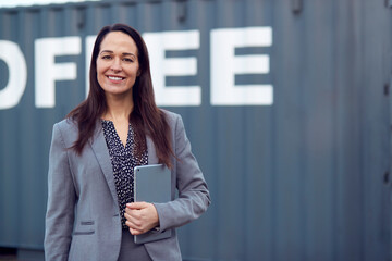 Portrait Of Female Freight Haulage Team Manager Standing By Shipping Container With Digital Tablet