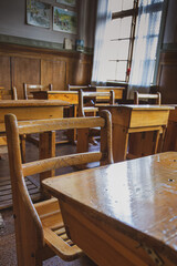 Vertical shot of a classroom in the art school with wooden desks and chairs and a big window