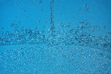 Pattern or pattern of frost and snowflakes on frozen glass of window. Christmas back. Macrophotography. Flat empty snow-covered surface of blue color.