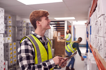 Male Worker Inside Busy Warehouse Checking Stock On Shelves Using Digital Tablet 