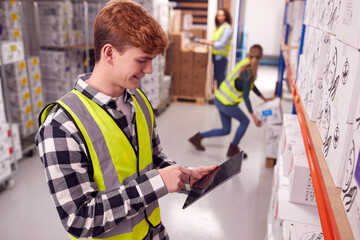 Male Worker Inside Busy Warehouse Checking Stock On Shelves Using Digital Tablet 