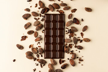 Chocolate bar top view on a light background surrounded by roasted cocoa beans
