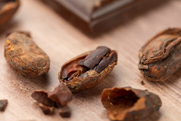Roasted and opened cocoa bean on the light wooden background with a piece of chocolate in the second plan. Close up picture, macrophotography.