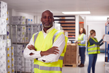 Portrait Of Team Male Leader In Warehouse With Staff Picking Items From Shelves In Background
