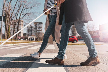 A blind male person using a white cane and walks with his female friend.They walk down the...