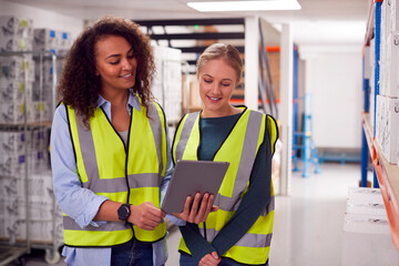 Female Team Leader With Digital Tablet In Warehouse Training Intern Standing By Shelves