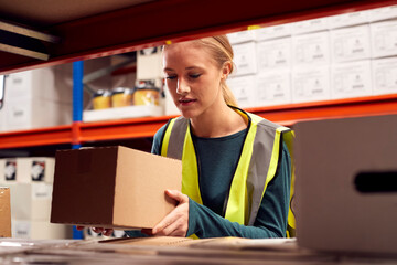 Female Worker Picking Box From Shelf Inside Warehouse 