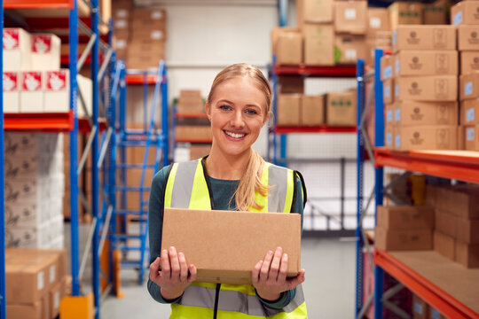Portrait Of Female Worker Holding Box Inside Warehouse 