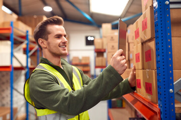 Male Worker Wearing Inside Warehouse Scanning Stock Barcode On Shelves Using Digital Tablet