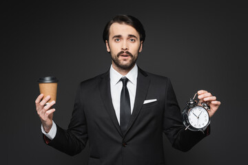 businessman with mustache holding paper cup and alarm clock on dark grey.