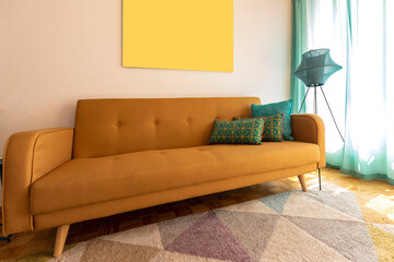 Mustard sofa detail with turquoise cushions and modern lamp. There is a painting on the wall