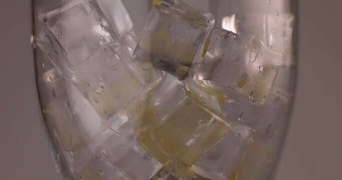 closeup pouring orange juice flowing through ice cube filling up a rotating glass