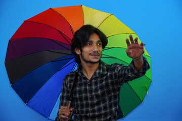 Young handsome man holding colorful umbrella and giving amazed expression, fear and excited face.