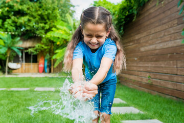 Cute girl popping water balloons in hands. Joint games with water for kids. Summer fun outdoor activities for children concept.