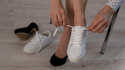 Close-up business woman takes off her shoes puts on white leather sneakers.