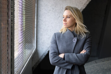 Blond woman with arms folded looking out of window