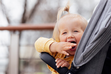 Sweet caucasian baby girl one year old sitting in stroller outdoors at spring. Little child in pram. Infant kid sits in pushchair. Autumnal walks with kids. Family leisure with little child.