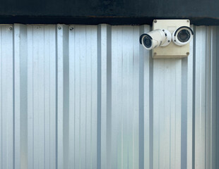 Two white CCTV cameras mounted  next to a black steel beams. wall for the background the galvanized sheet Installing