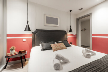 Bedroom with king size headboard with cushions, studded gray fabric upholstered headboard, red and white painted walls and wardrobe with gray sliding doors, bedside tables and twin pendant lamps