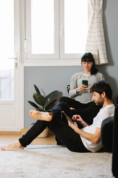 Man using tablet near pregnant wife browsing smartphone in apartment