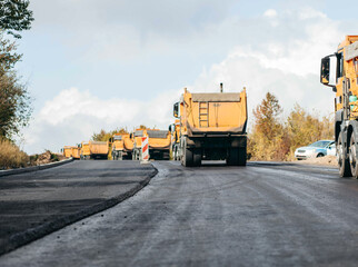 Many trucks with hot asphalt are waiting in line for unloading. Road service repairs the highway, background