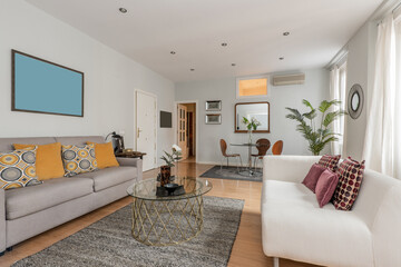 Contemporary decor living room with white and gray sofas with lots of colorful cushions, rugs and a circular glass dining and coffee table