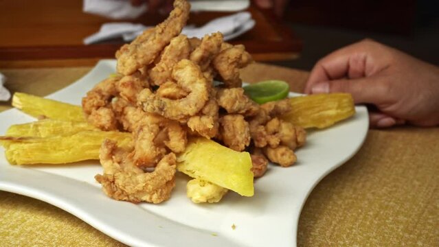 closeup of a plate of fried fish chicharron with yucca and lemon in a marine restaurant on the beach in the day in 4k