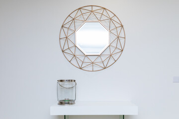 Mirror in the form of a polygon with a round golden halo on the outside hangs over the nightstand