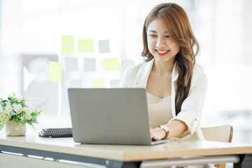 Portrait of Asian young businesswoman with laptop writes on a document at her office,Asian girl working at a office space with a laptop computer. 